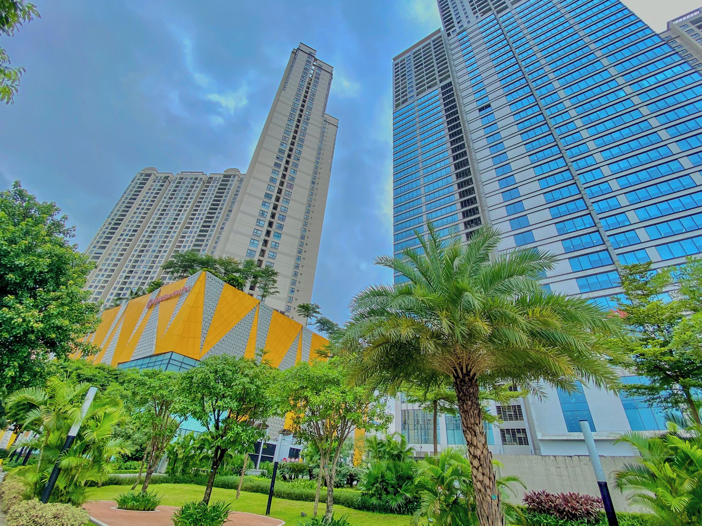 A modern building complex with high-rise structures and a well-maintained garden area with palm trees.