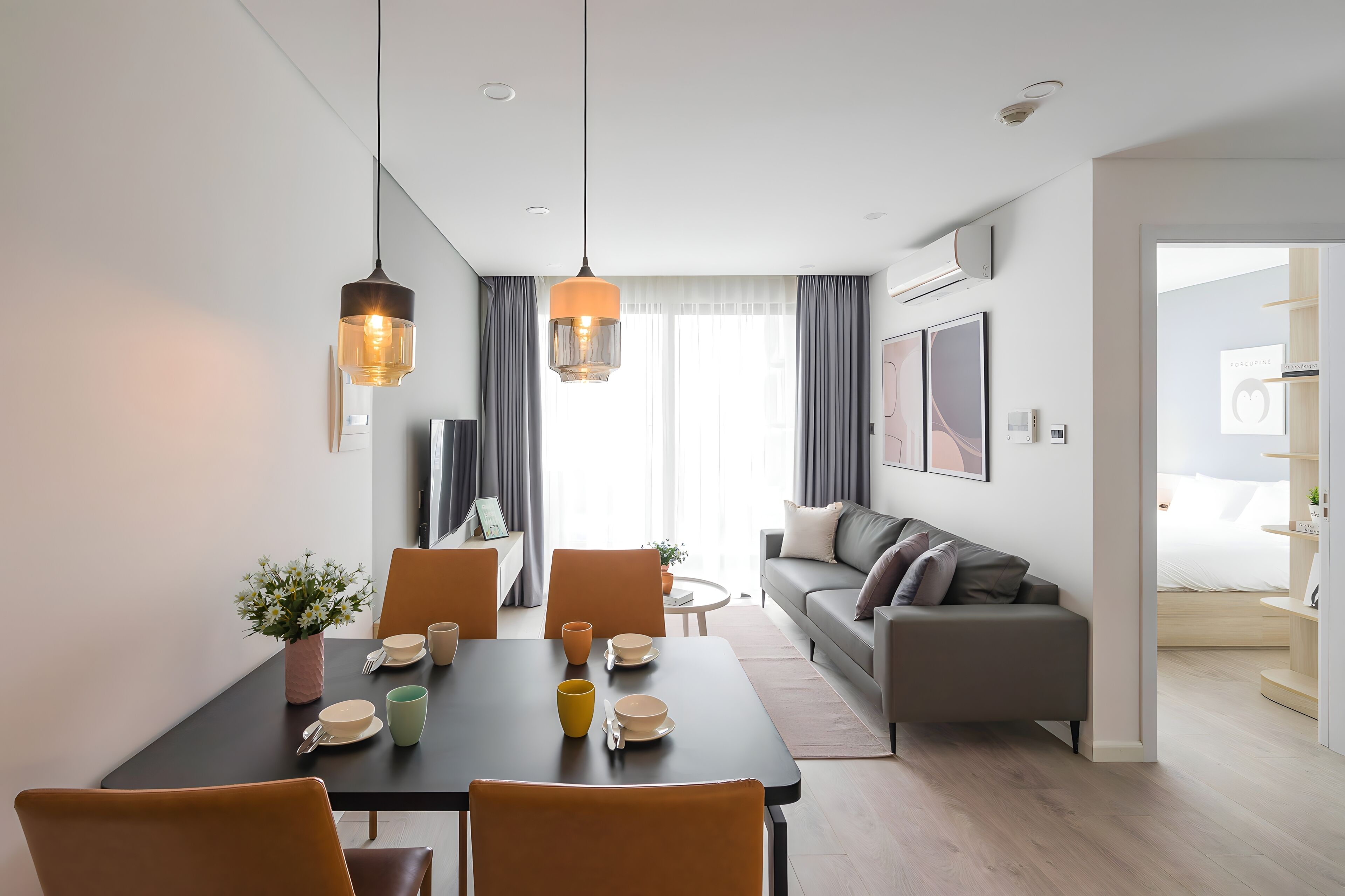 A modern living room with a dining area, featuring a sofa, a coffee table, and a dining table set with plates and cups.