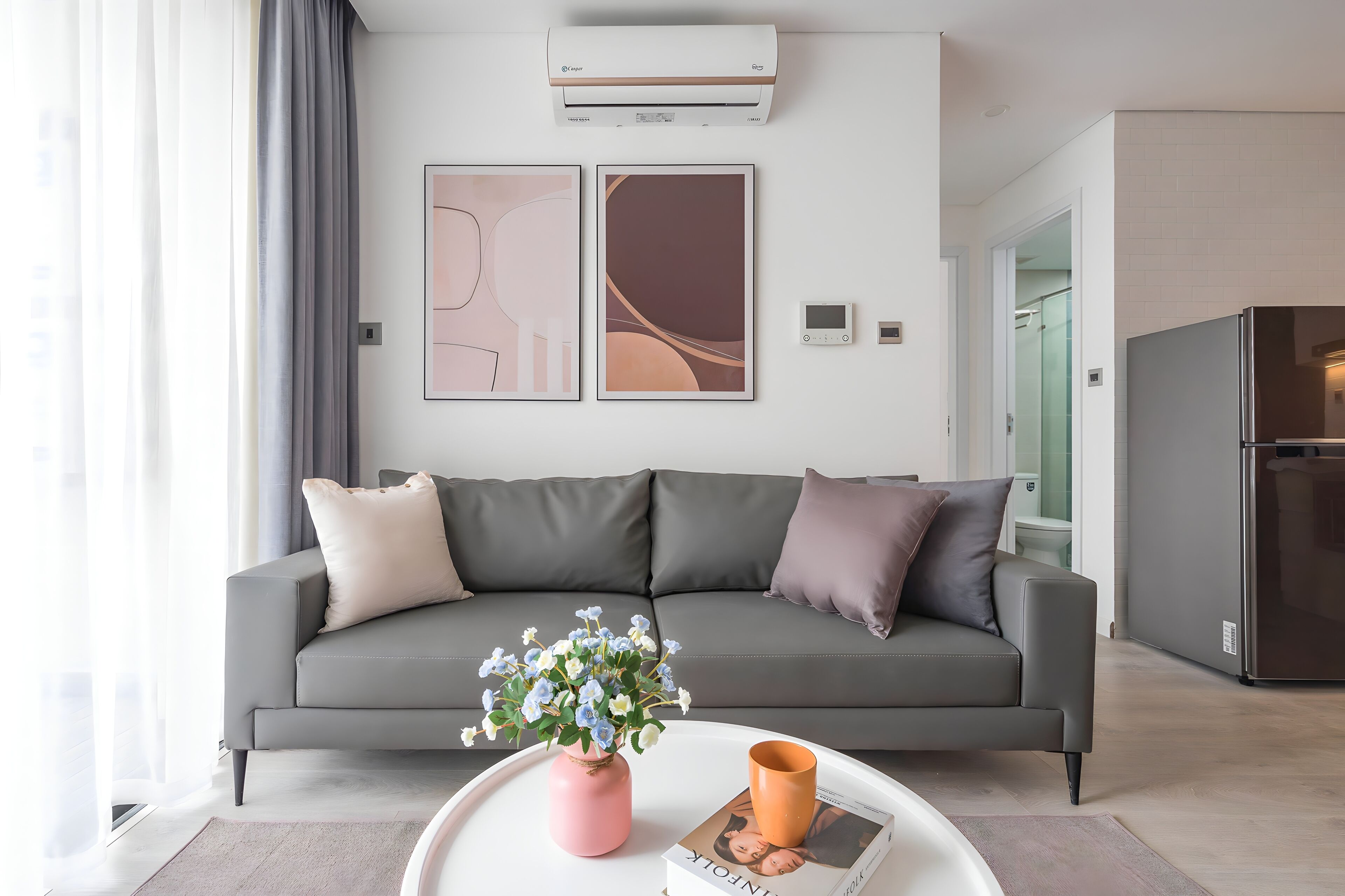 A modern living room with a grey sofa, a pink vase with flowers, and a coffee table with a book and a mug.