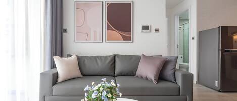 A modern living room with a grey sofa, a pink vase with flowers, and a coffee table with a book and a mug.