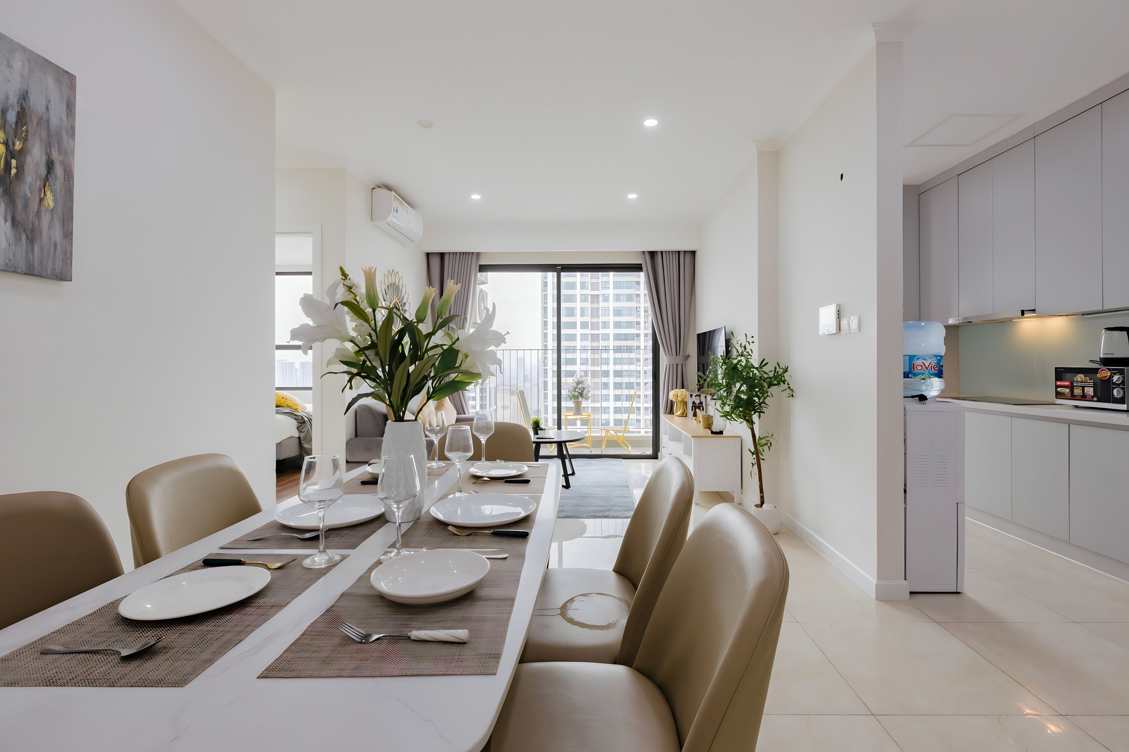 Un comedor moderno con una mesa preparada para cuatro, una cocina con armarios grises y un ventanal con cortinas.