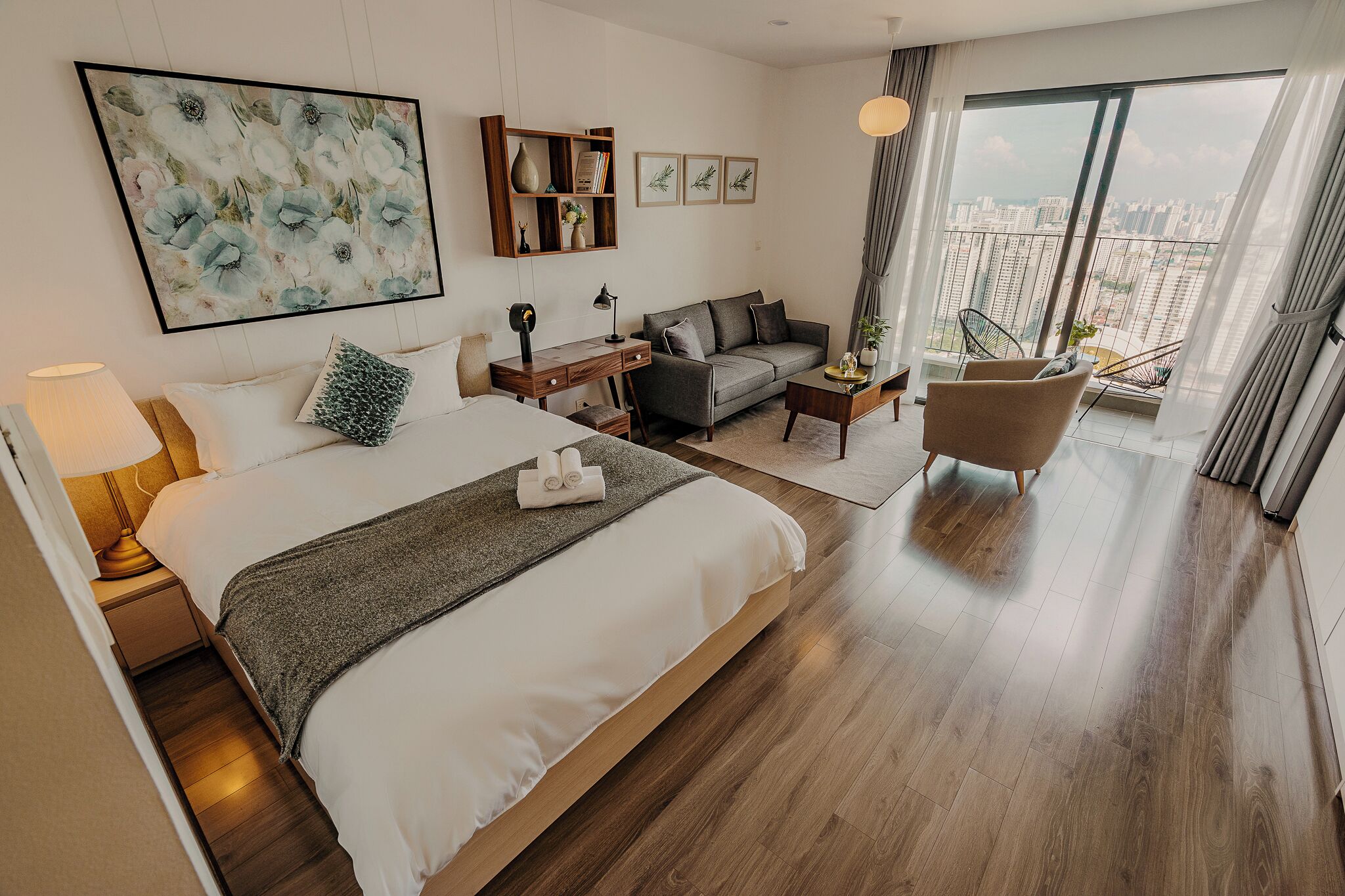 Une chambre d’hôtel avec un grand lit, un canapé, un bureau et une chaise. Une grande fenêtre offre une vue sur les bâtiments.
