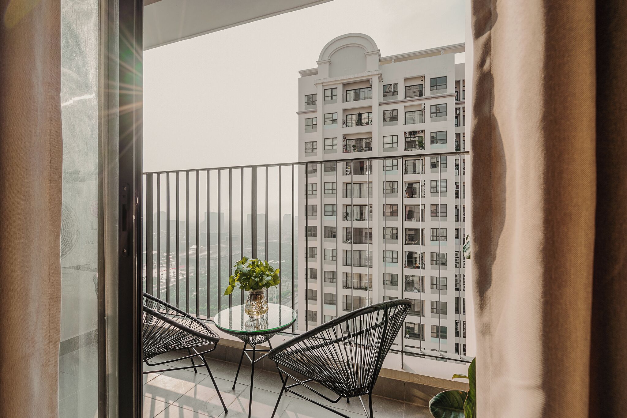 A balcony with a glass table and chairs, a potted plant, and a view of a high-rise building.