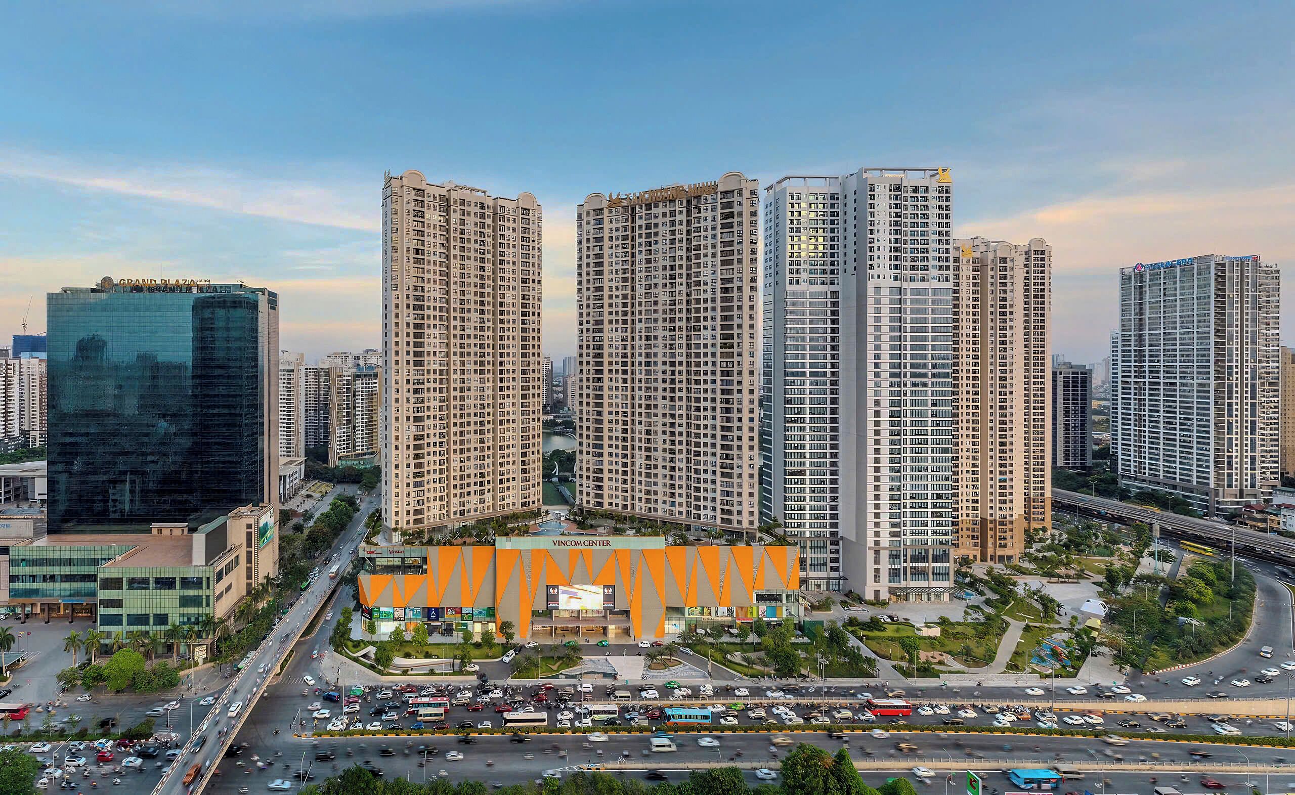 A high-rise residential building complex with multiple apartment buildings, a central commercial building, and a busy urban street with vehicles.