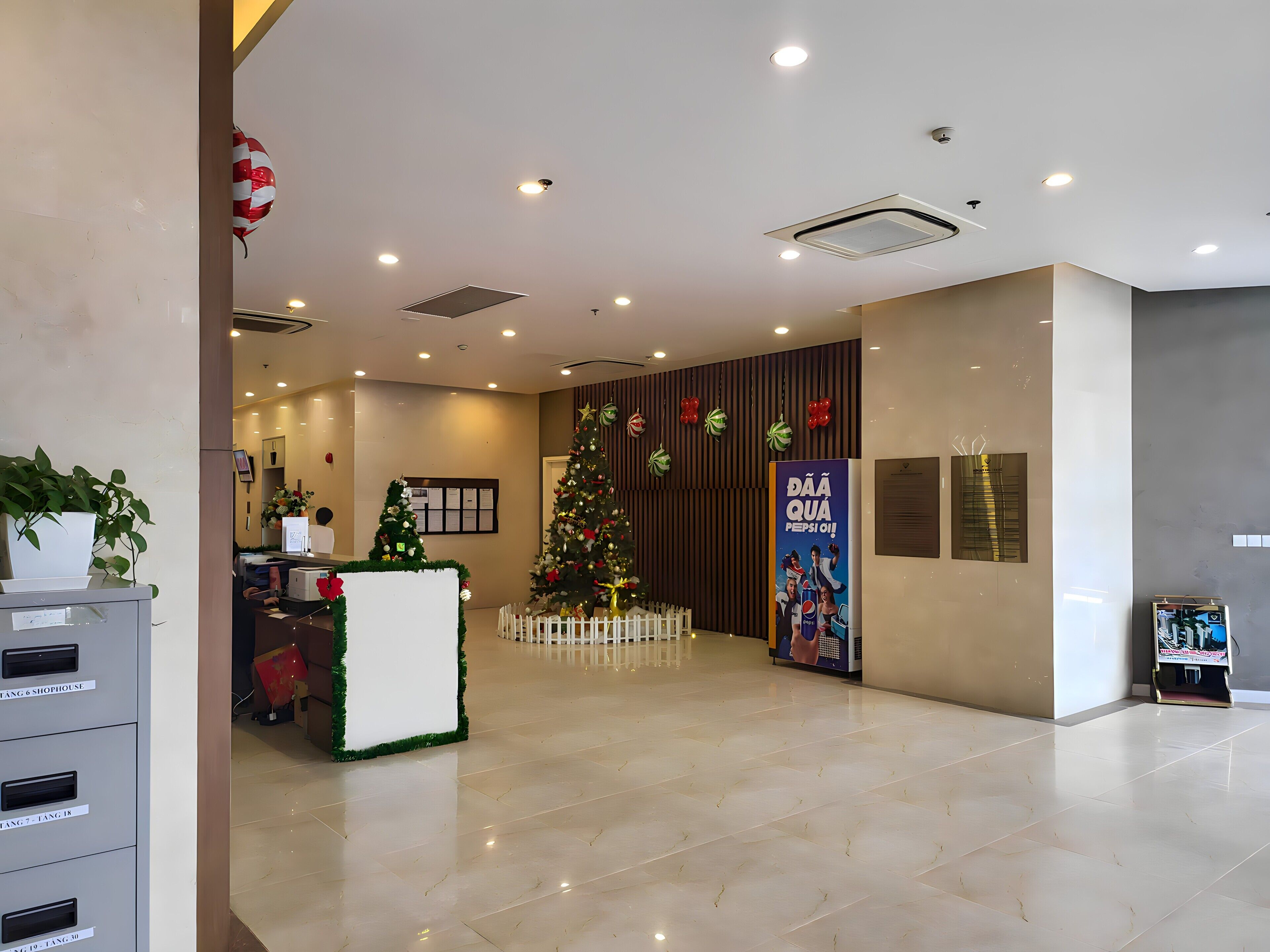 A hotel reception area with a Christmas tree, a large poster, and a plant.