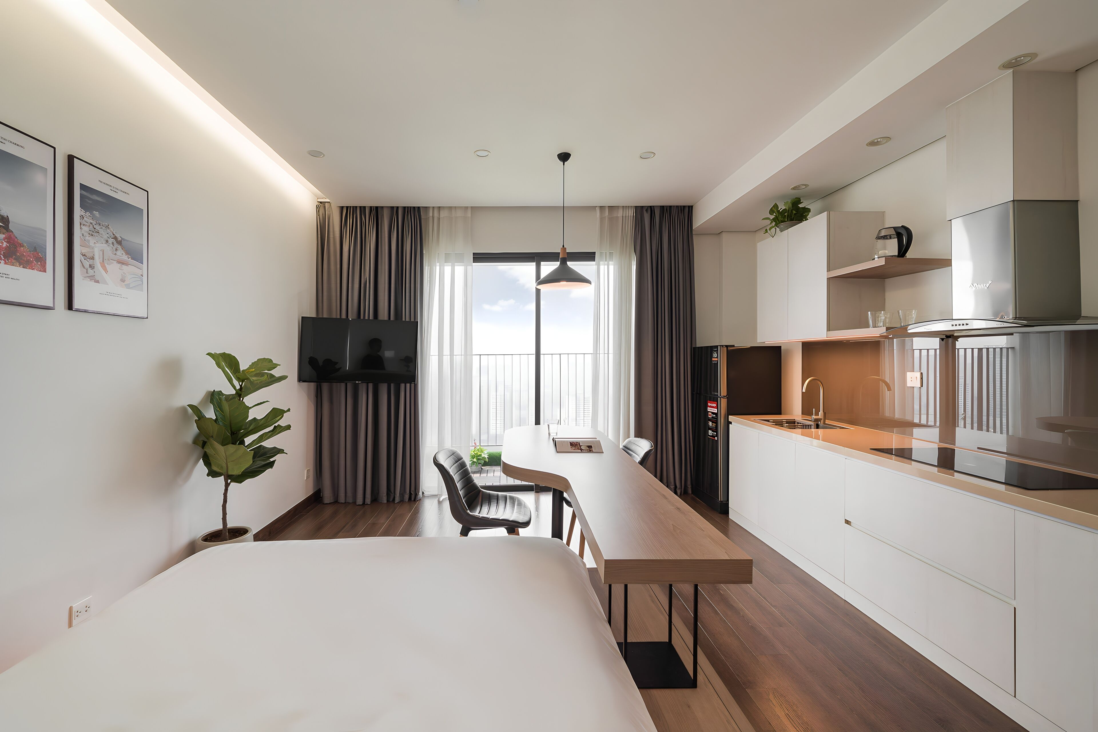 A modern hotel room with a bed, a desk, a chair, a TV, a plant, a window with curtains, and a kitchenette.