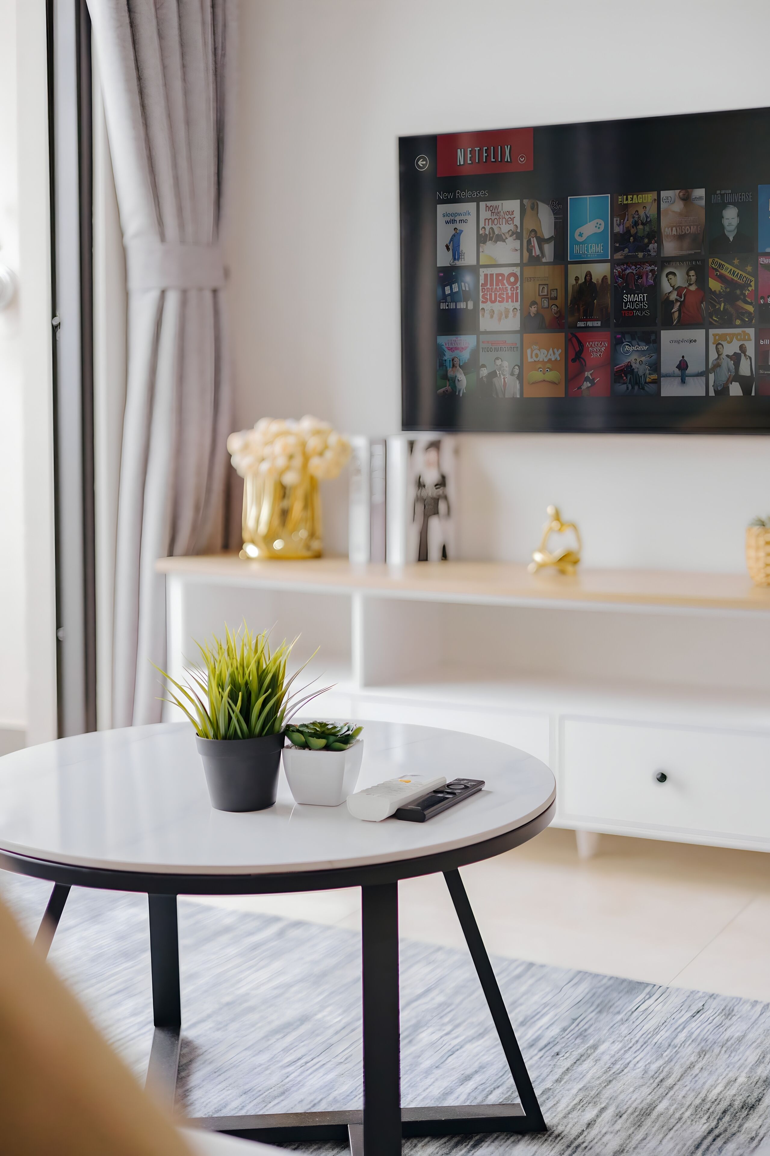 Un salon moderne avec une table ronde, une plante en pot, une télécommande et un téléviseur fixé au mur qui diffuse les nouvelles sorties de Netflix.