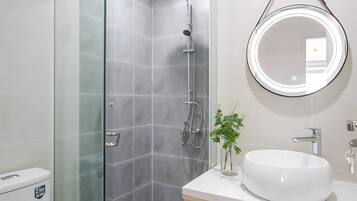 A modern bathroom with a glass-enclosed shower, a round mirror, a white sink, and a toilet.