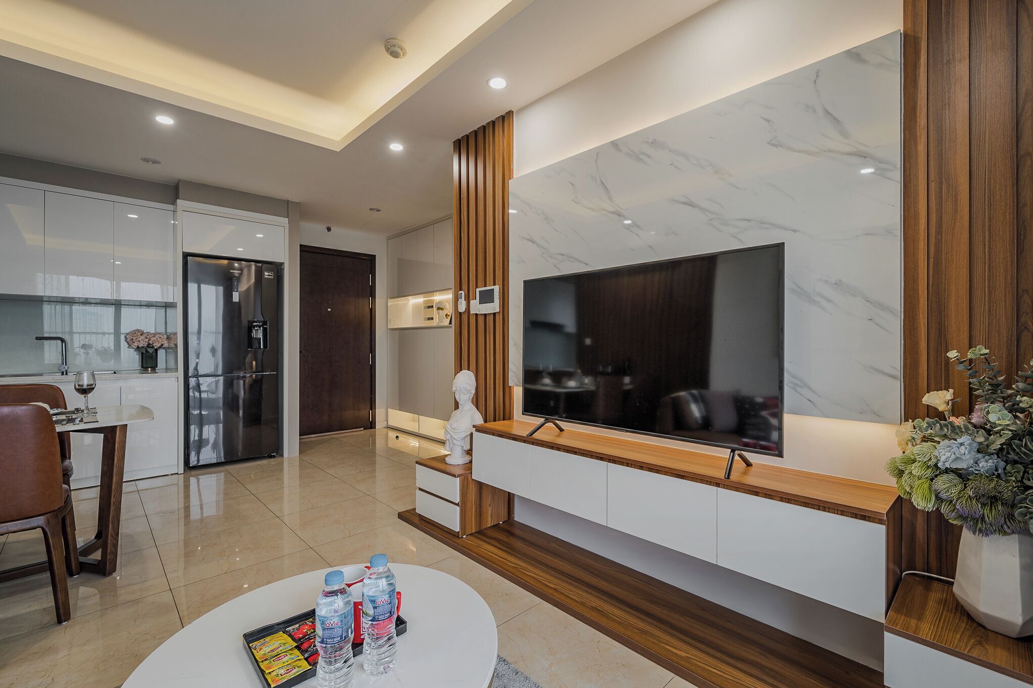 A modern kitchen with a built-in refrigerator, a dining area with a table and chairs, and a living area with a TV and decorative items.