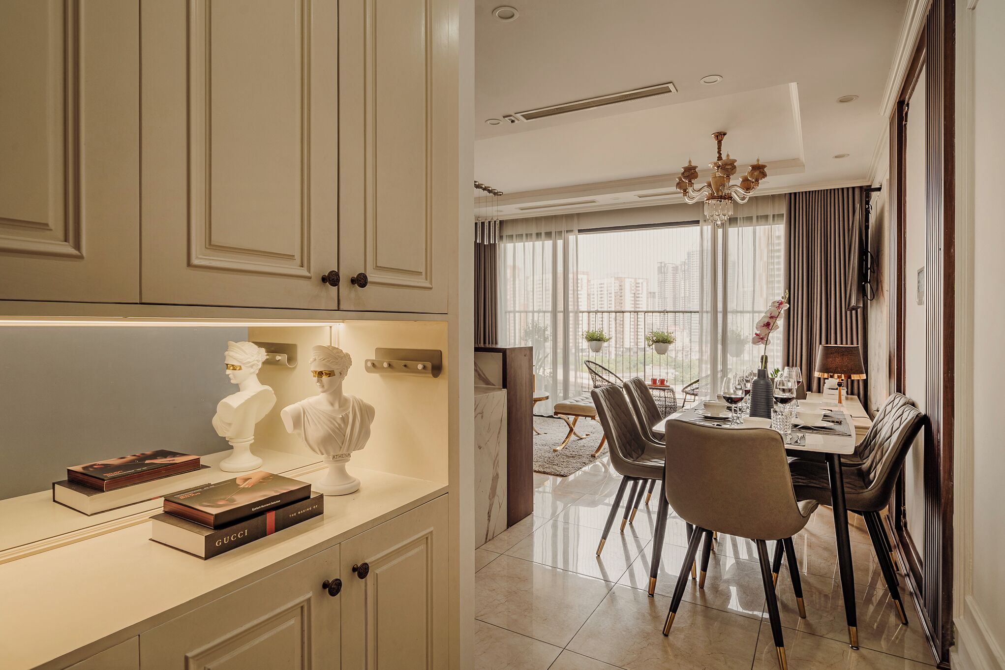 A modern dining area with a chandelier, dining table set for four, and a view of the city through large windows.