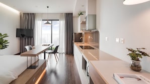 Une chambre d’hôtel moderne dotée d’un coin repas, d’une kitchenette et d’une grande fenêtre avec des rideaux.
