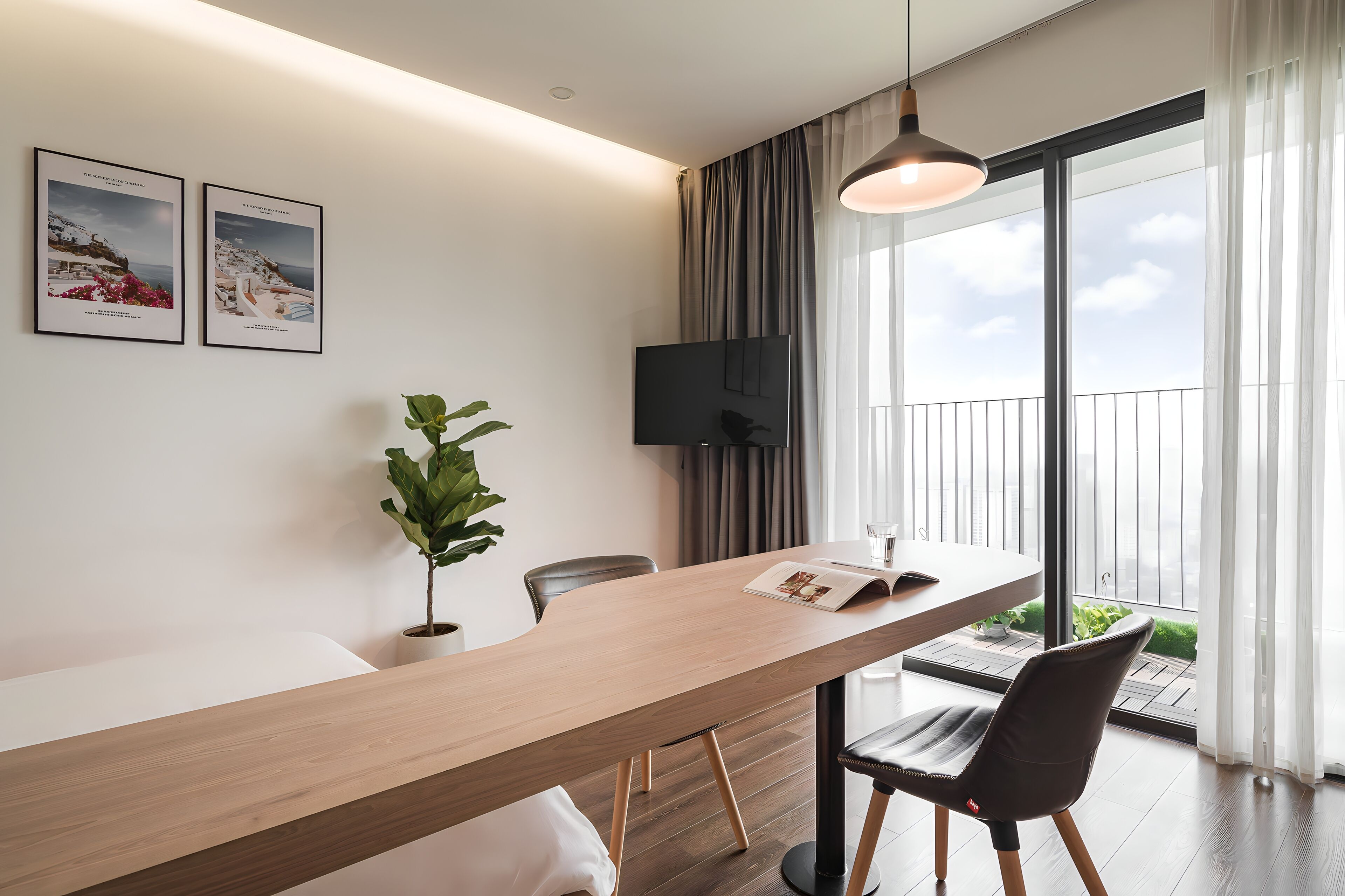 A modern room with a long wooden table, a potted plant, a flat-screen TV, and a view of the outdoors through large windows.
