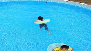 A swimming pool with two children floating on inner tubes. - Hotel O Sri Ayu Inn (Gurun)