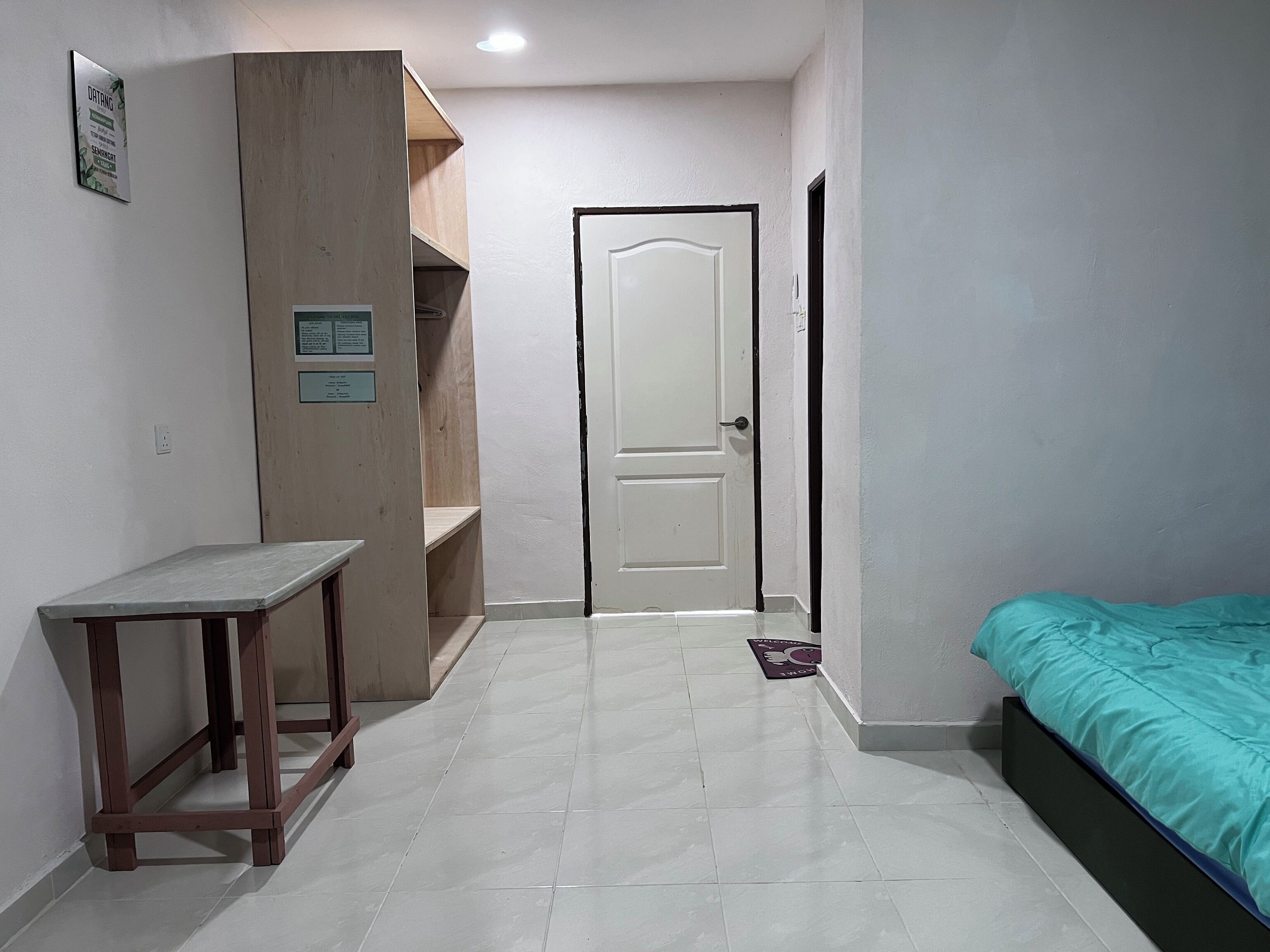 A small, clean room with a bed, a desk, and a door leading to another room.