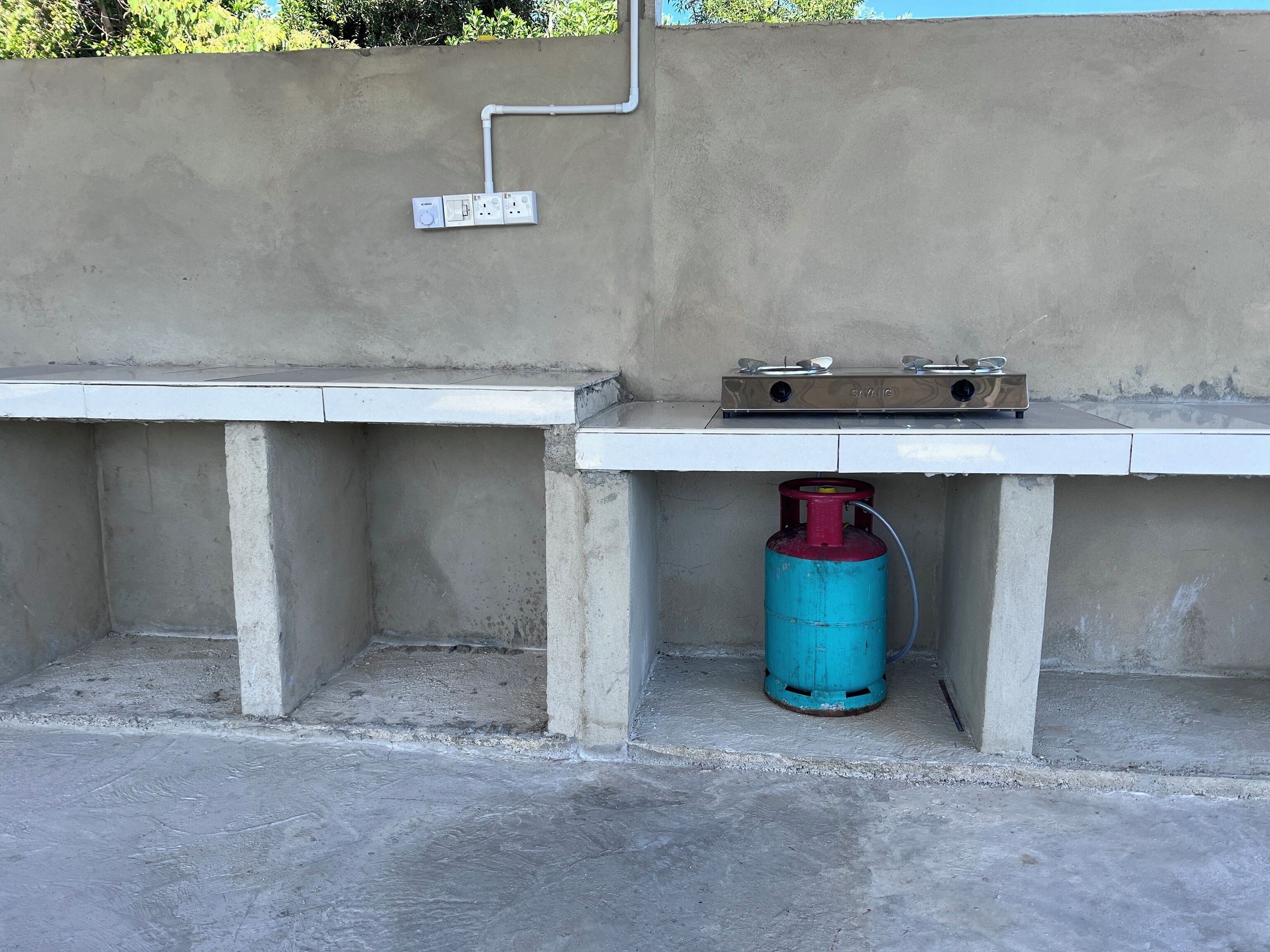 Un espace extérieur en béton comprenant une bouteille de gaz, une boîte métallique et des prises électriques fixées sur un mur.