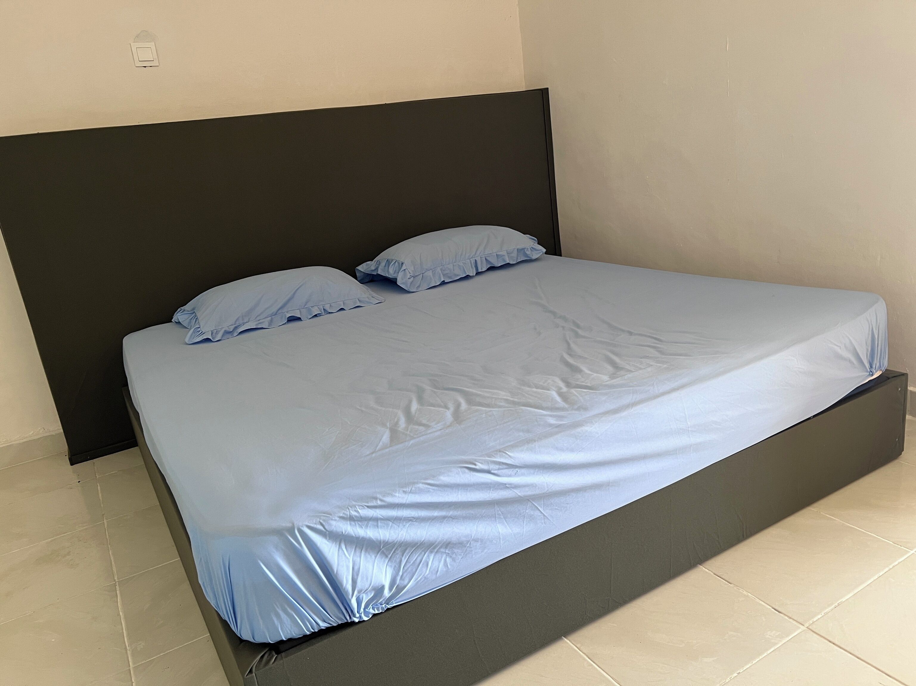 A bed with a dark headboard and a light blue mattress cover.