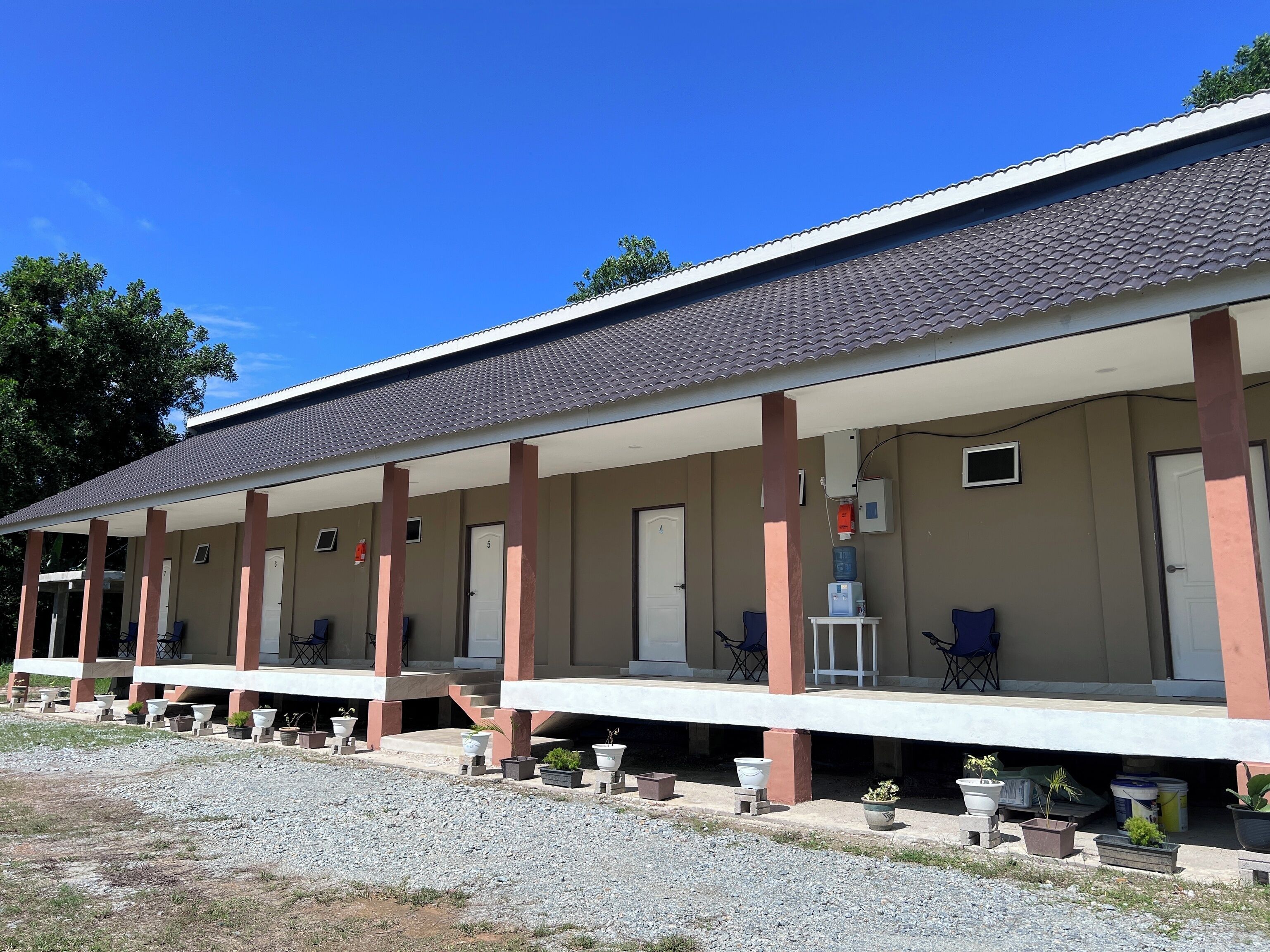 Un motel con área de estar al aire libre cubierta, habitaciones individuales con acceso directo y plantas en macetas.
