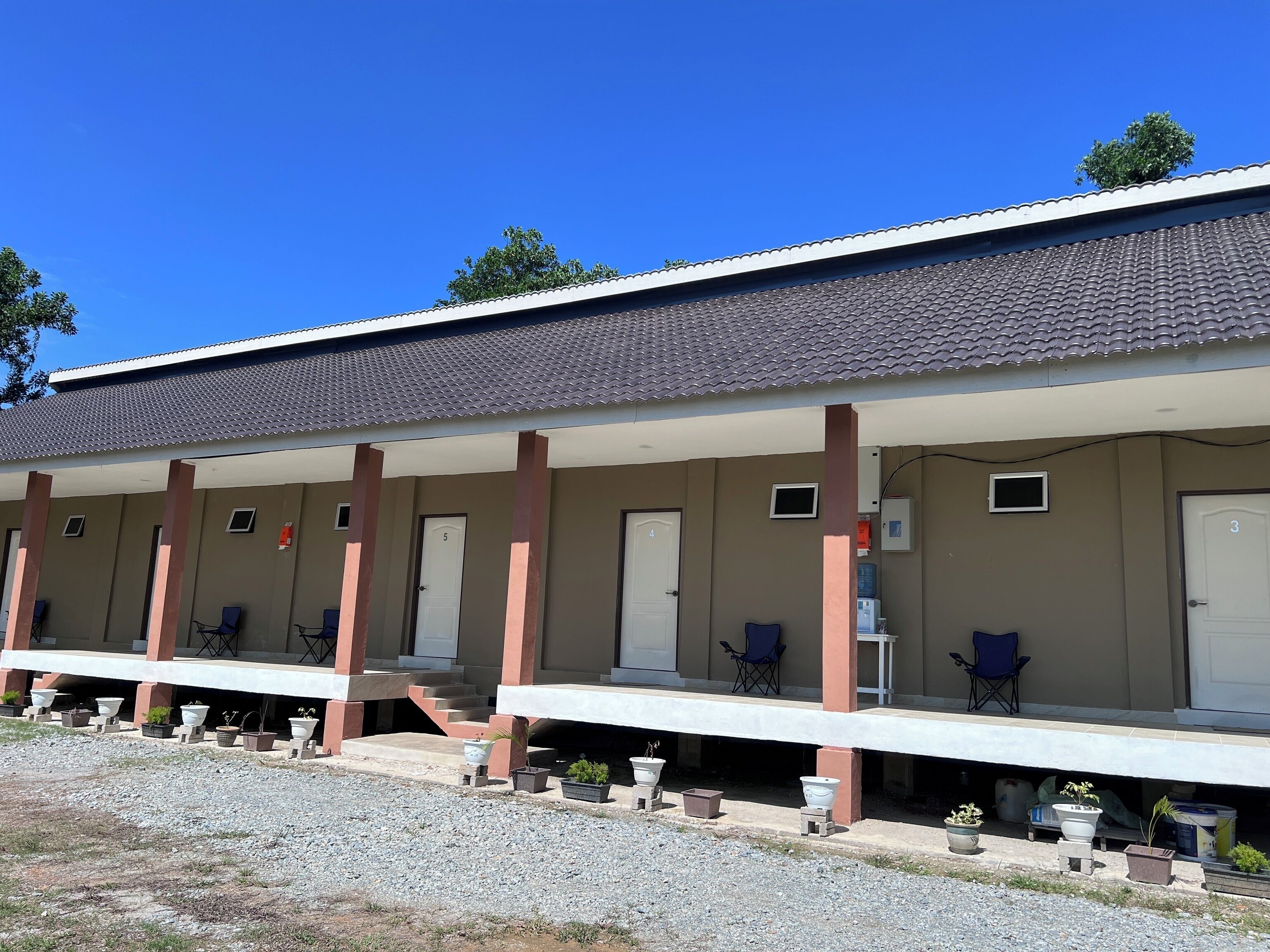 Un motel con zona de estacionamiento techada, varias habitaciones y plantas en macetas.