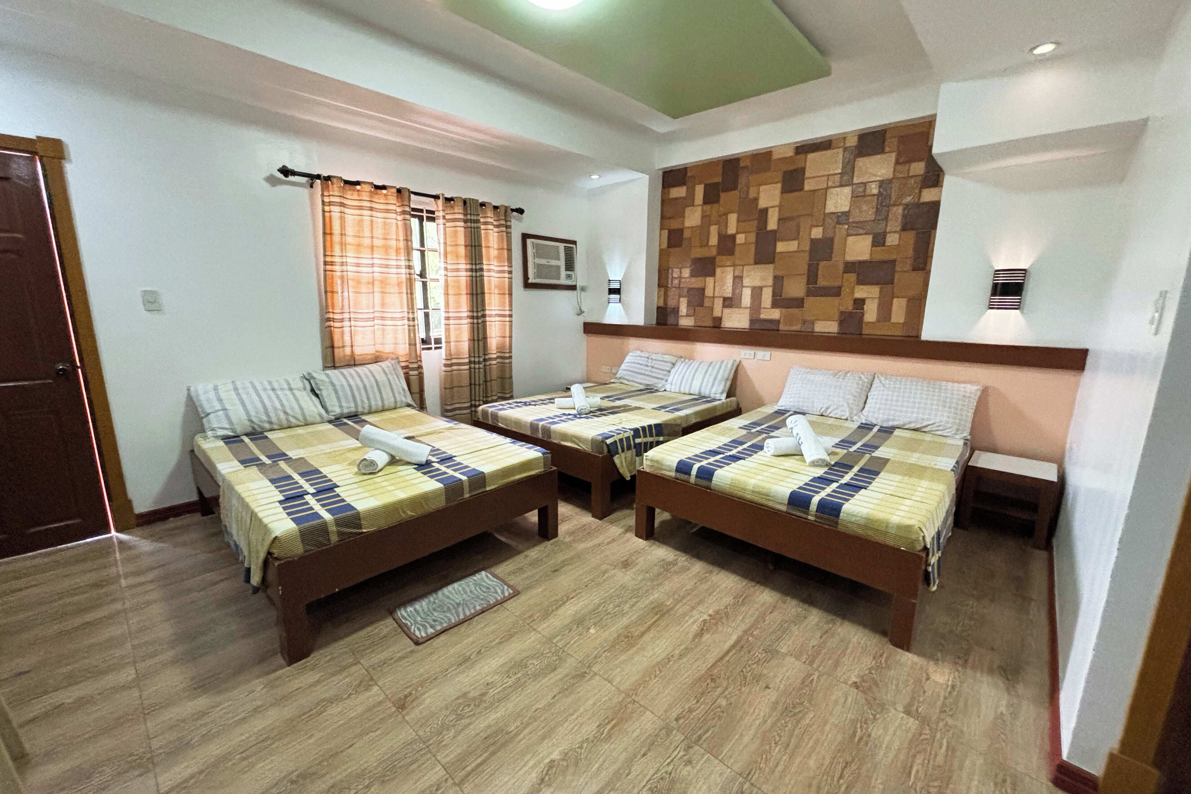 Una habitación con dos camas individuales, suelo de madera, una lámpara de pared y una ventana con cortinas.