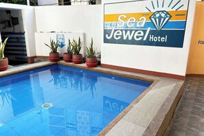 Une piscine entourée de plantes en pot et un panneau indiquant l’hôtel Sea Jewel.