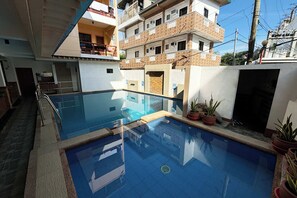 A swimming pool with a tiled deck, surrounded by potted plants and a multi-story building with balconies. -  Sea Jewel Hotel Puerto Galera powered by Cocotel (Puerto Galera)