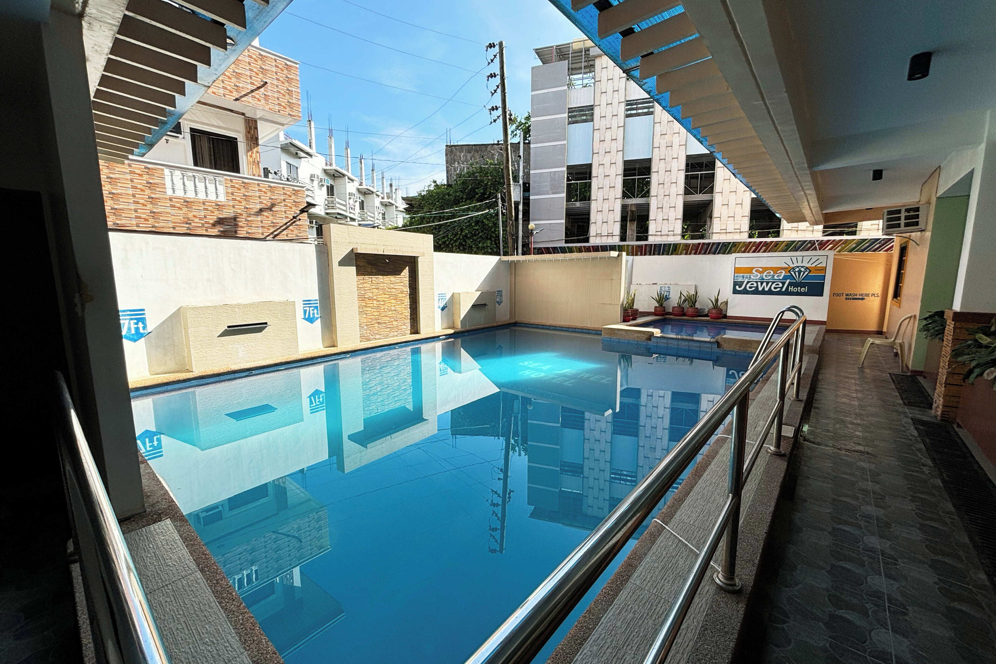 A swimming pool with a glass barrier, surrounded by buildings and a sign for Sea Jewel Hotel.