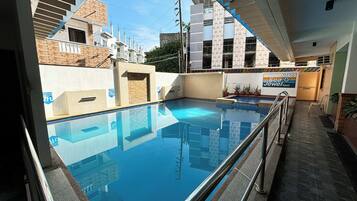 A swimming pool with a glass barrier, surrounded by buildings and a sign for Sea Jewel Hotel.