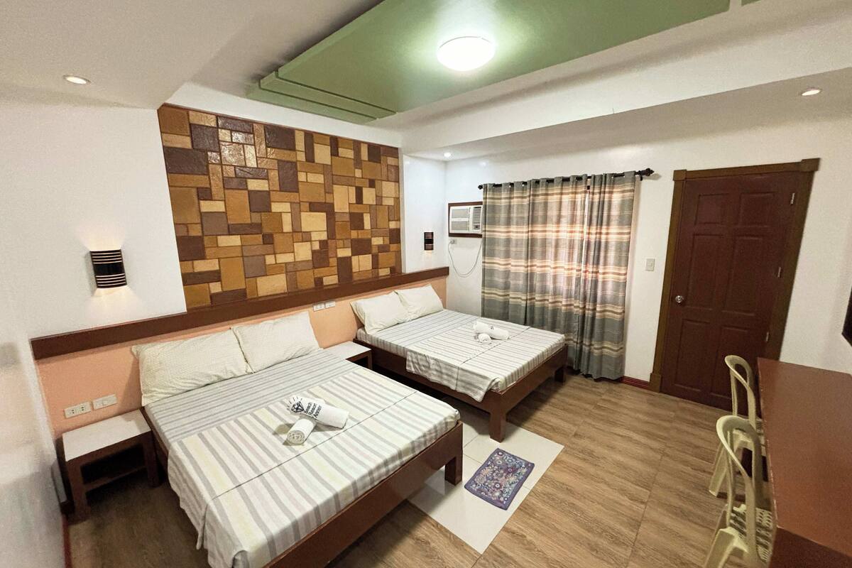 Une chambre d’hôtel avec deux lits, une tête de lit en bois, un climatiseur fixé au mur, une fenêtre avec des rideaux et une porte.