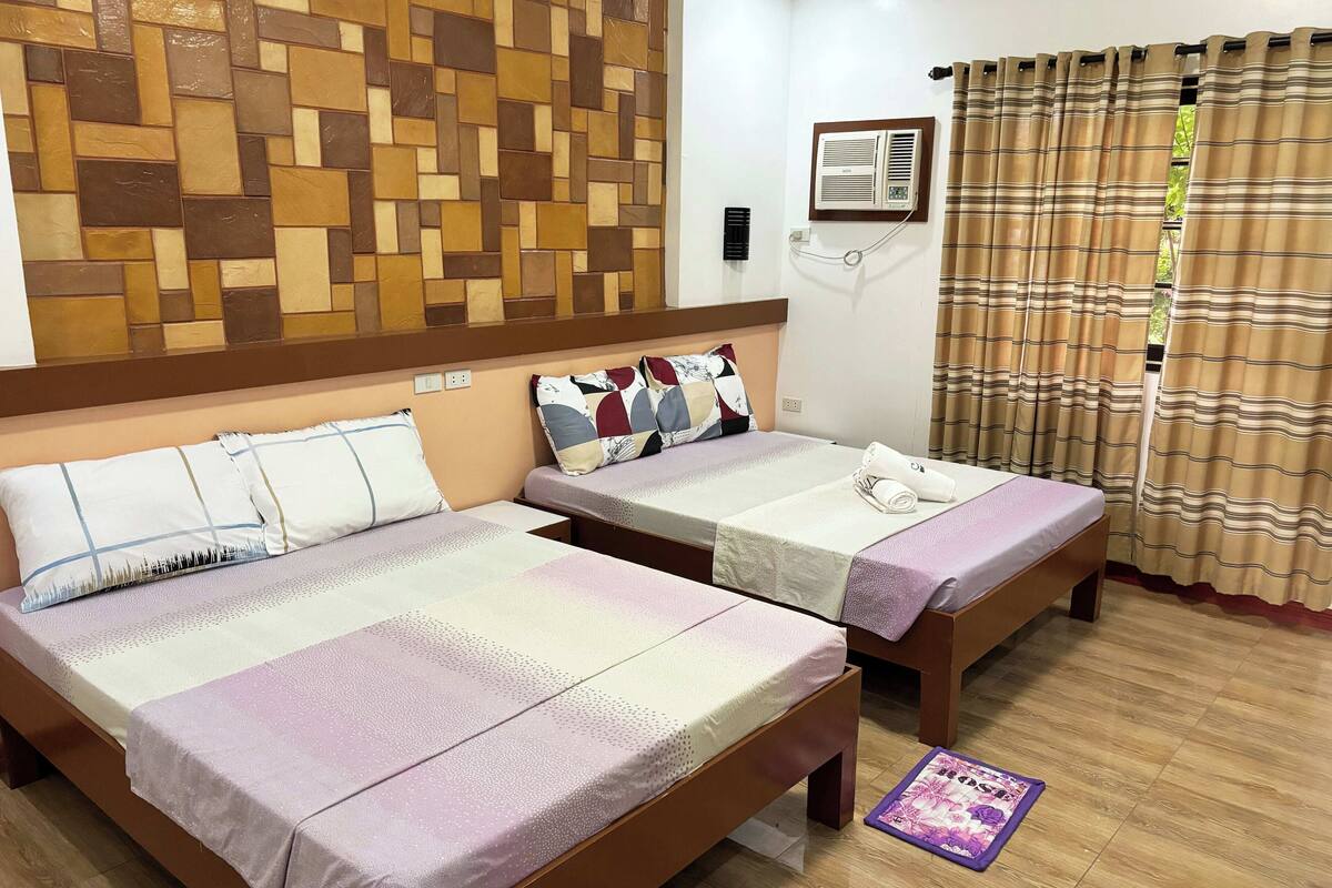 Une chambre d’hôtel avec deux lits, un mur orné d’un motif géométrique, un appareil de climatisation et une fenêtre avec des rideaux.