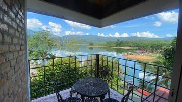 A balcony with a table and chairs, overlooking a lake and mountains.