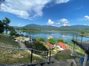 A scenic view of a lake with mountains in the background, a red-roofed building, and outdoor seating areas. - Collection O 91015 Sungai Batang Lake Chalet (Kampung Sungai Batang)