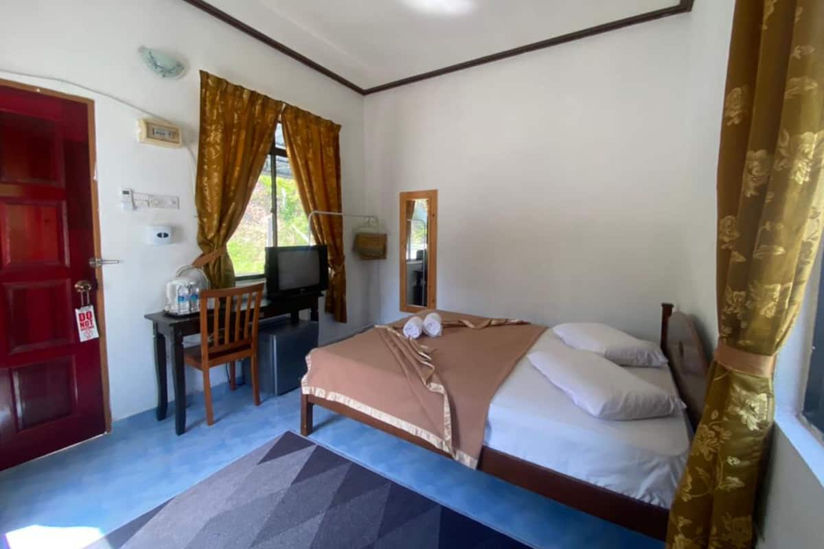 A bedroom with a bed, a desk with a television, a red door, and a window with curtains.