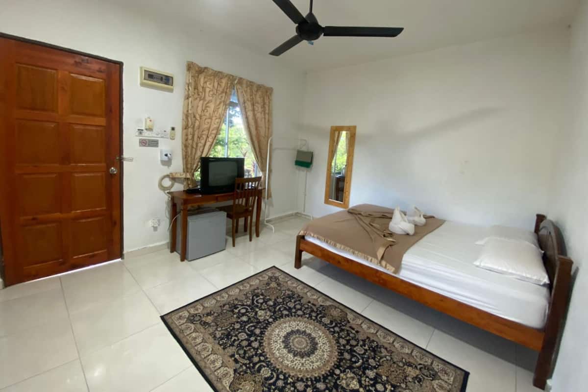 A bedroom with a bed, a desk with a television, a ceiling fan, a window with curtains, and a door.