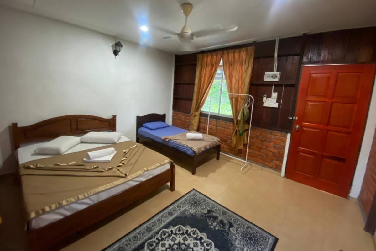 A bedroom with two beds, a ceiling fan, a window with curtains, a red door, and a patterned rug.