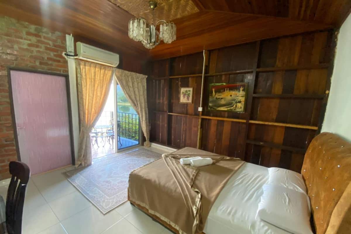 A bedroom with a bed, a chair, a window with curtains, a wooden wall, and a painting.