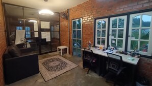 Une pièce avec un mur en briques, une grande fenêtre, un bureau et une chaise.