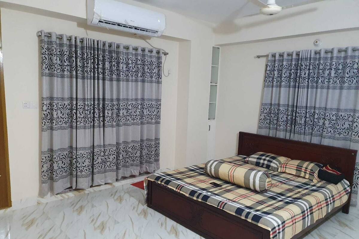 Un dormitorio con cama, cortinas, aire acondicionado y ventilador de techo.