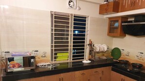 Une cuisine avec des meubles de rangement en bois, un four à micro-ondes, une fenêtre avec des stores et une cuisinière.