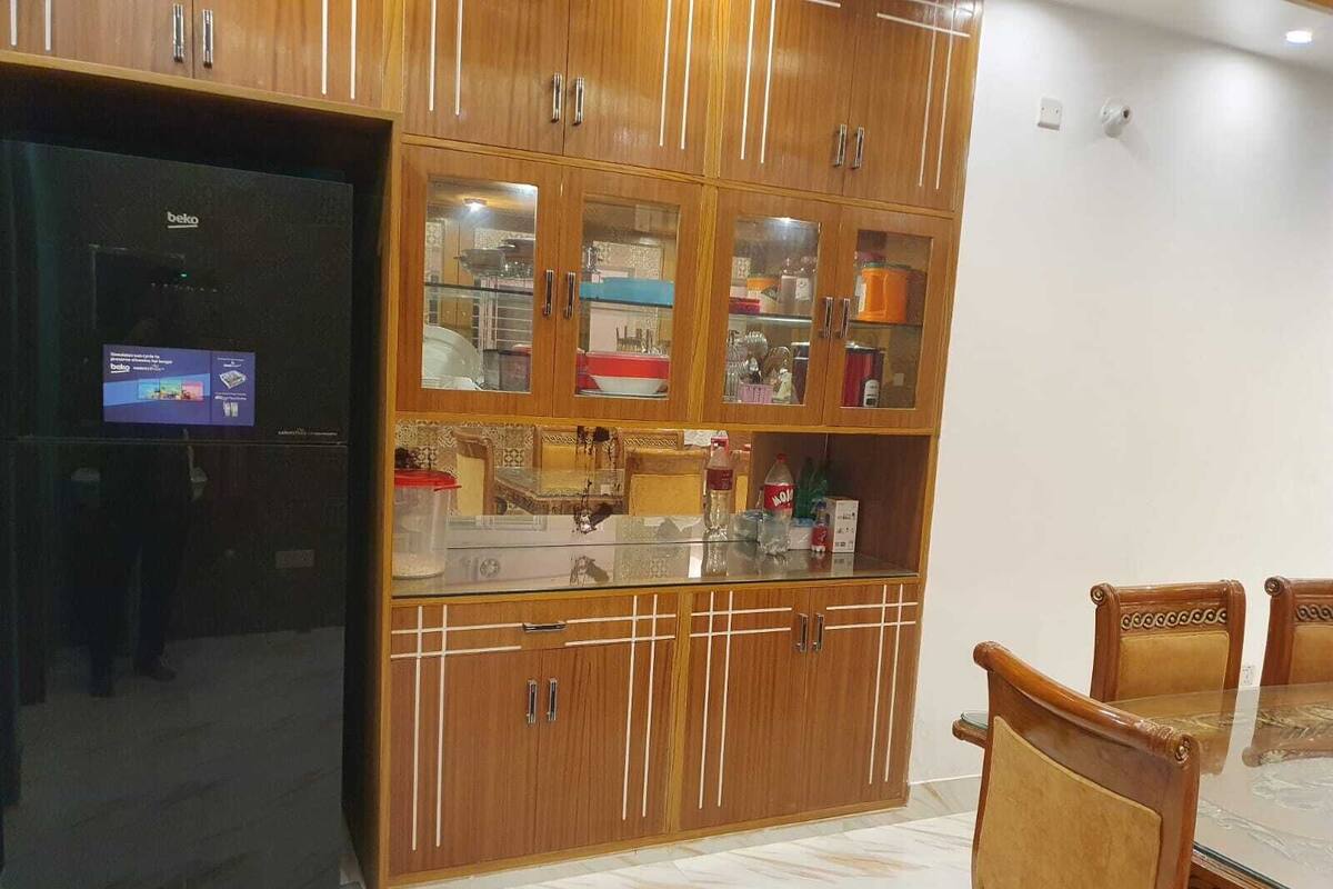 Una cocina con armarios de madera, un refrigerador negro y una mesa de comedor con cubierta de vidrio y sillas.