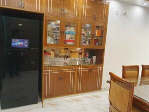 A kitchen with wooden cabinets, a black refrigerator, and a glass-top dining table with chairs. - Roop Kothar Rajjo (Keraniganj)