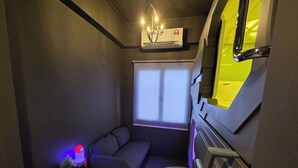 A compact room with a grey sofa, a small table with a lamp, a window with blinds, and a staircase with a yellow accent. - Space Hotel KL Sentral (Kuala Lumpur)