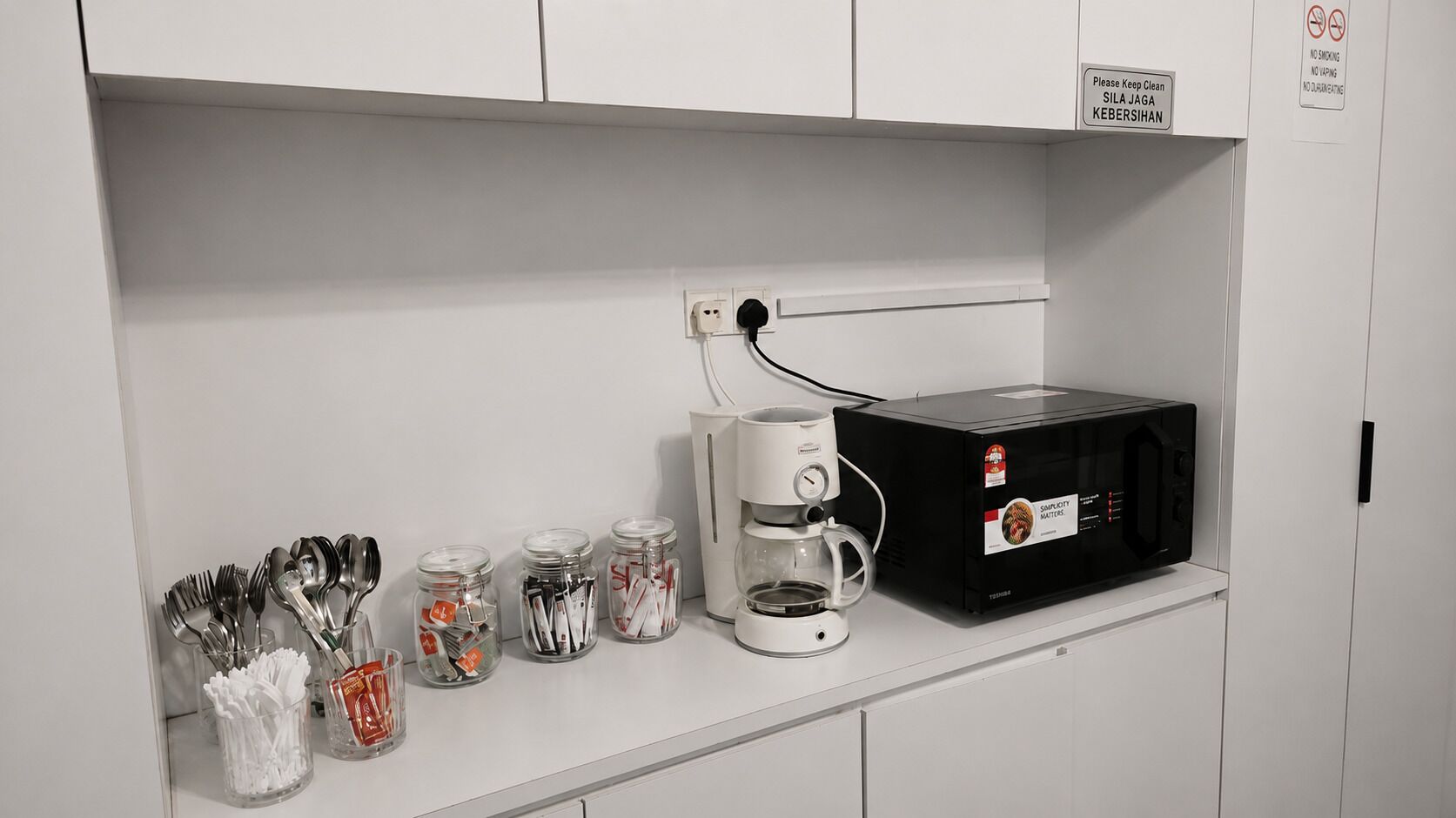 A kitchenette with a microwave, coffee maker, and utensils stored in jars.