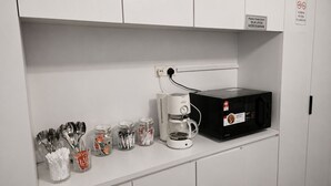 Uma cozinha compacta com micro-ondas, cafeteira e utensílios guardados em potes.
