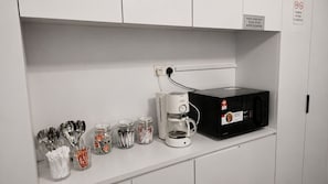 A kitchenette with a microwave, coffee maker, and utensils stored in jars. - Space Hotel KL Sentral (Kuala Lumpur)