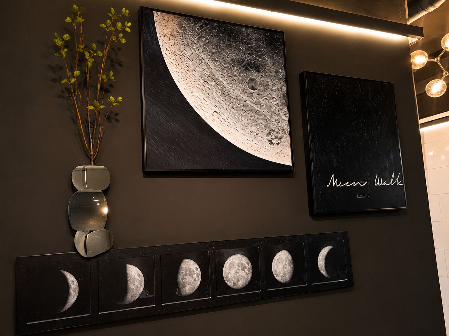 Uma parede com uma grande obra de arte representando as fases da lua, uma moldura menor com texto, e uma fileira de impressões das fases da lua.