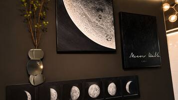 Uma parede com uma grande obra de arte representando as fases da lua, uma moldura menor com texto, e uma fileira de impressões das fases da lua.