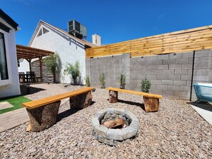 An outdoor patio with two wooden benches, a stone fire pit, and a pergola. - Firepit & Friends Modern, Intimate Backyard & More (Phoenix)