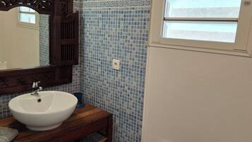 Une salle de bain avec un lavabo blanc, un miroir avec un cadre en bois et des carreaux de mosaïque bleus sur le mur.