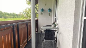 A covered outdoor area with a table and chairs, a wooden railing, and a view of greenery.