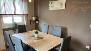 A dining area with a wooden table, grey upholstered chairs, a potted plant, and a wall-mounted sign. - Apartment 'Wohner' with Private Garden, Balcony and Wi-Fi (Petersaurach)